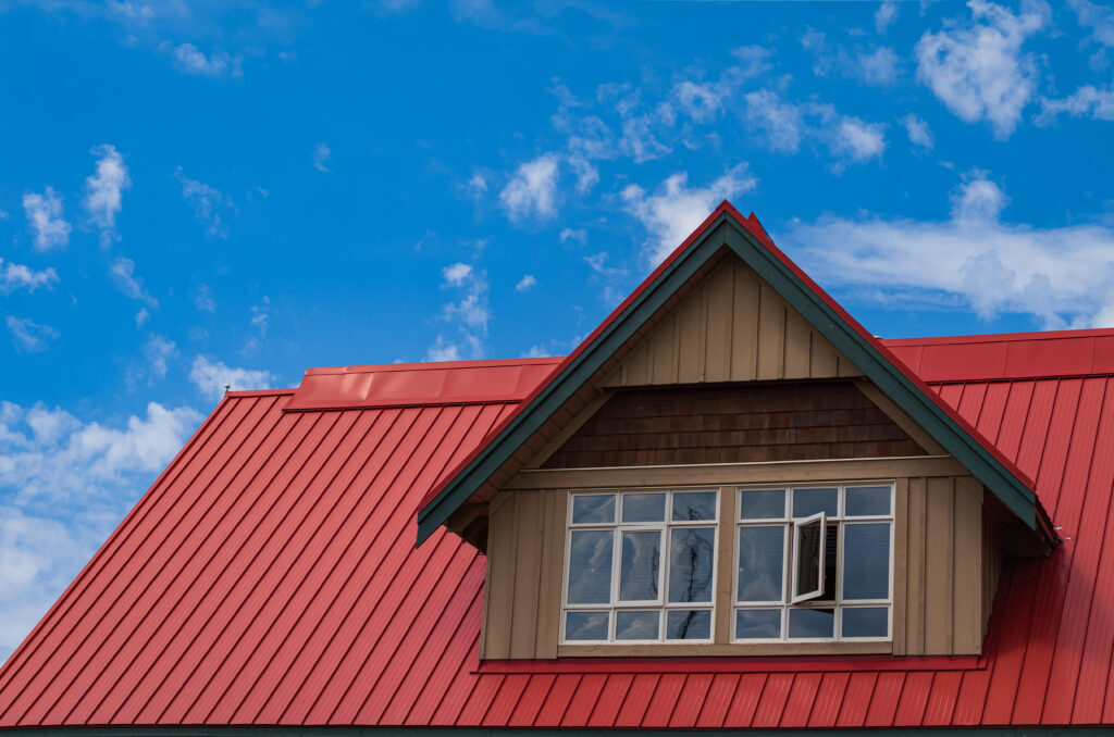 Red roof on a home with tan siding and white windows 