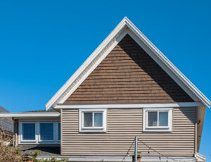 Tan home with roof shingles on top of the house against blue sky